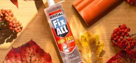 Soudal Fix All High Tack Clear klej montażowy - tuba na drewnianym stole w otoczeniu jesiennych liści i owoców jarzębiny, obok fragmentu pomarańczowego elementu wykończeniowego.