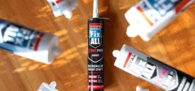 Kartusz kleju Soudal Fix All X-Treme Power umieszczony centralnie na drewnianym blacie, otoczony rozłożonymi promieniście innymi tubami klejów Fix All. Zdjęcie z góry w promieniach słońca.