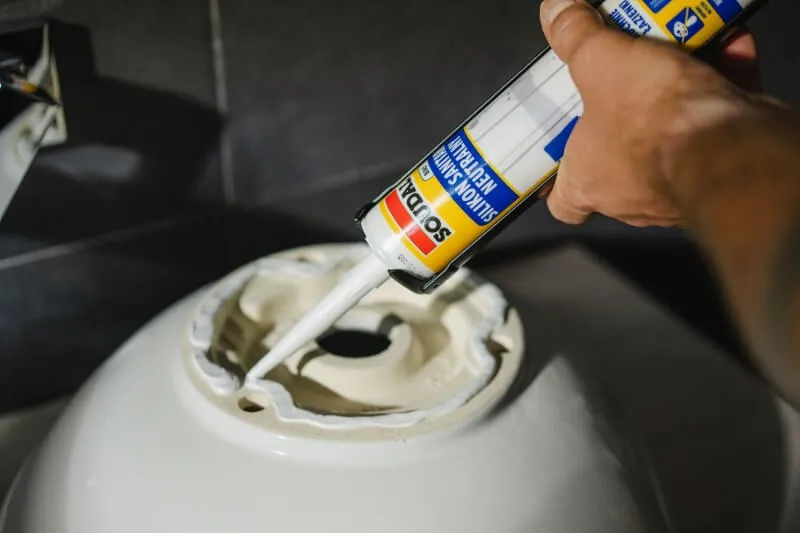 Mężczyzna aplikuje silikon sanitarny Soudal pod umywalkę łazienkową