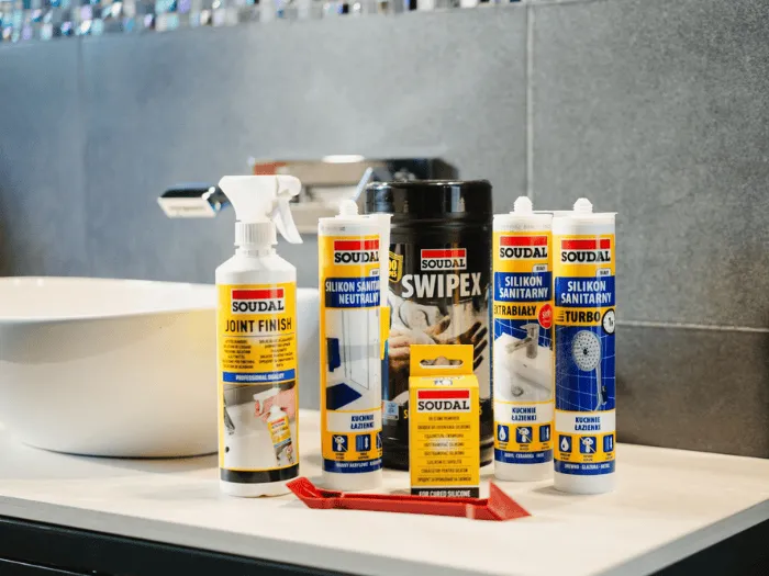 Produkty Soudal do uszczelniania łazienek: silikony sanitarne, preparat Joint Finish oraz chusteczki Swipex na blacie łazienkowym.