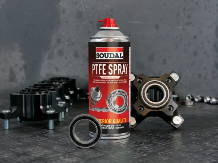 Aerozol techniczny PTFE Spray marki Soudal stoi na blacie wśród metalowych elementów mechanicznych