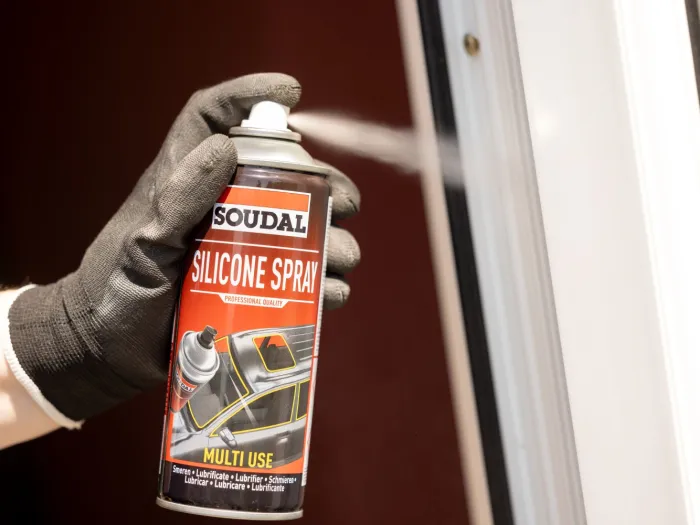 Męska dłoń w rękawicy ochronnej spryskuje uszczelkę okna za pomocą Silcone Spray firmy Soudal