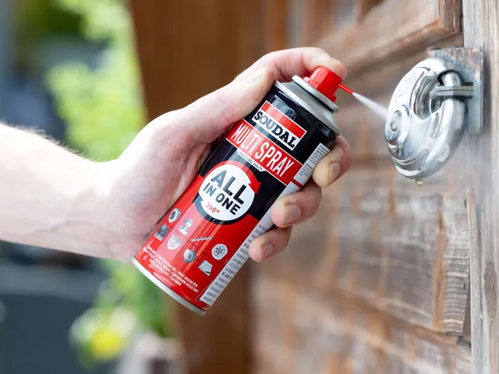 Męska dłoń spryskuje mechanizm kłódki za pomocą Multi Spray firmy Soudal