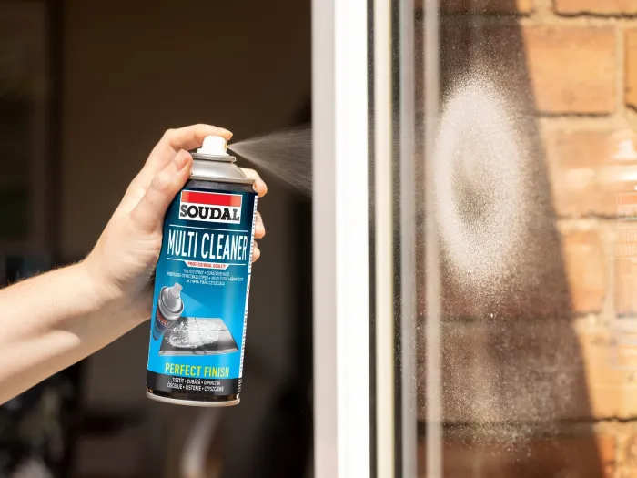 Ręka trzyma puszkę aerozolu Multi Cleaner, którym myje okno  w domu