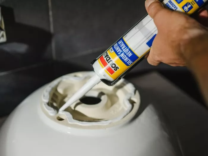 Mężczyzna aplikuje silikon sanitarny Soudal pod umywalkę łazienkową