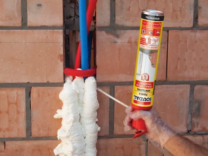Wypełnianie bruzdy instalacyjnej z peszlami w ścianie z pustaków ceramicznych przy użyciu niskoprężnej pianki montażowej Soudal Genius Gun.