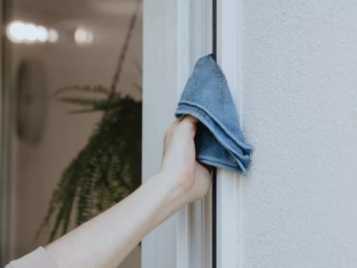 Dłoń kobiety myje framugę okna niebieską ściereczką
