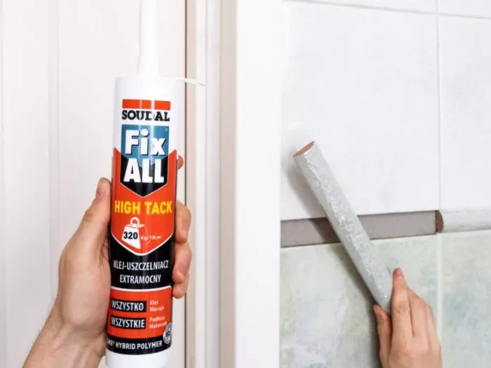 Mężczyzna trzyma w jednej dłoni klej fix all high tack, natomiast w drugiej kawałek płytki do przyklejenia