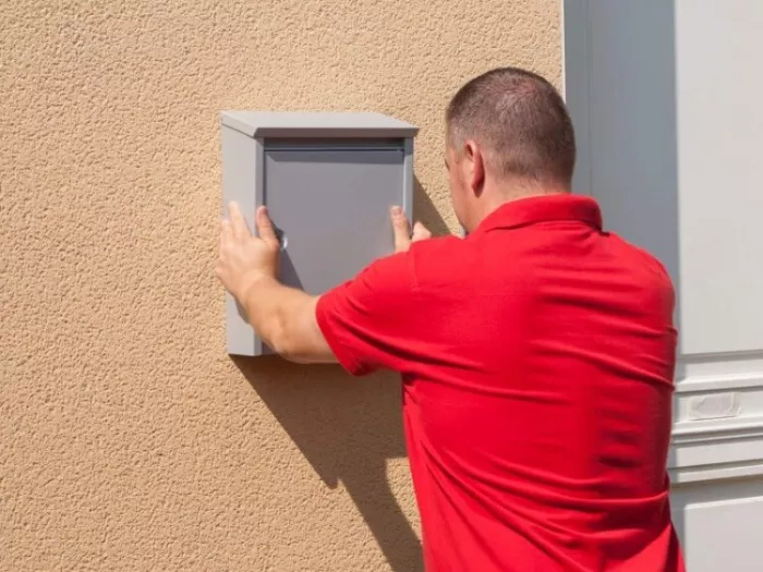 Mężczyzna przykleja metalową skrzynkę na listy