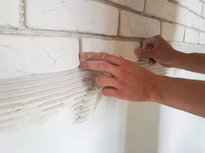 Ręce przyklejają płytki gipsowe do ściany