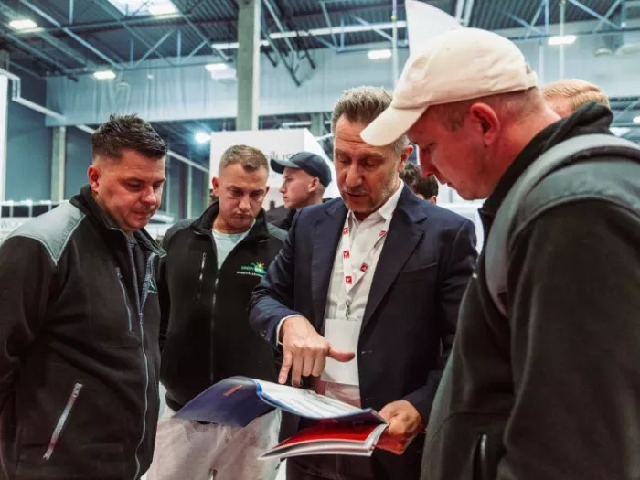 Grupa mężczyzn omawiająca materiały drukowane i katalog produktów podczas targów branżowych.